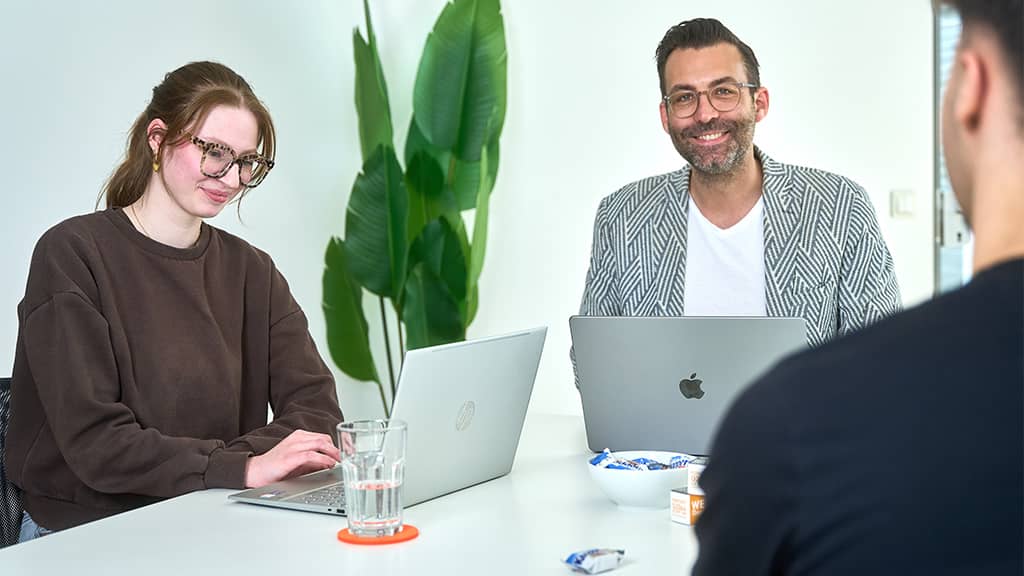 Drei Personen mit Laptops besprechen im Agenturbüro Strategie und Planung für einen Onlineshop.