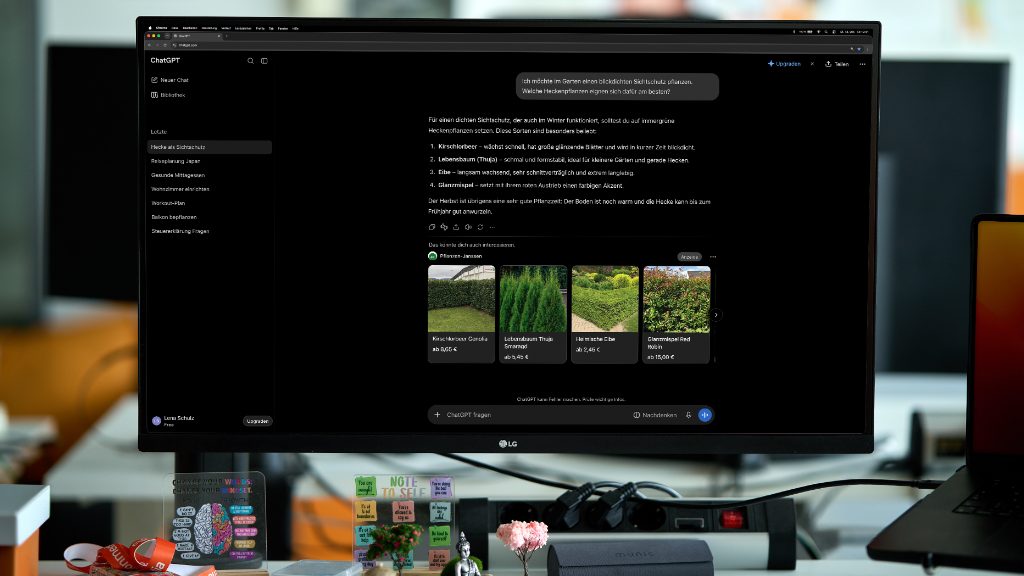 Monitor zeigt auf einer ChatGPT-Seite Produktkarten für Heckpflanzen und Gartenangebote in einer Büroumgebung.
