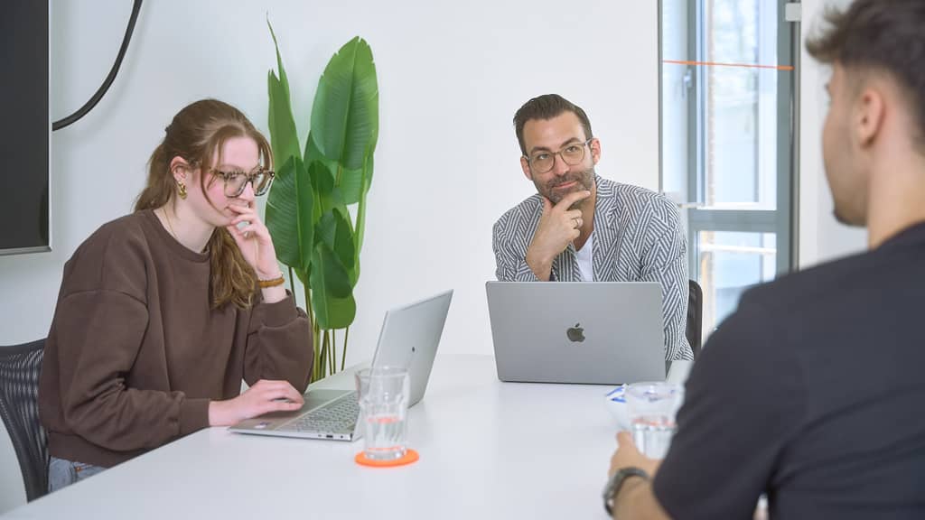 Zwei Teilnehmende mit Laptops hören einem Sprecher zu, während sie Notizen und Gedanken austauschen.