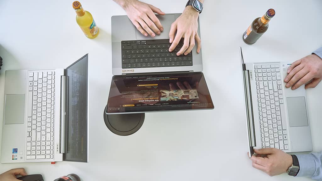 Top-Down-Aufnahme von Händen an Laptops während der Planung einer Suchmaschinenwerbung-Kampagne.