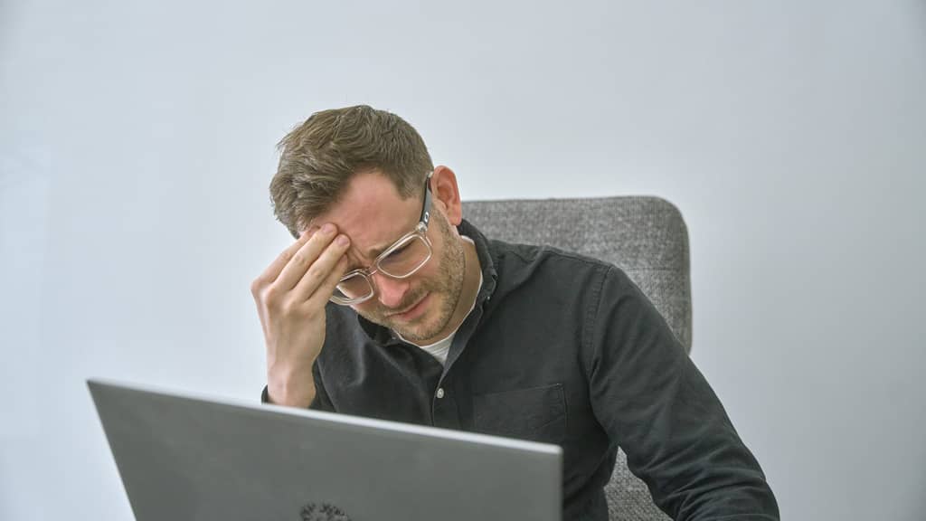Mann mit Brille sitzt vor Laptop und wirkt gestresst beim Überprüfen einer Google Shopping Kampagne.