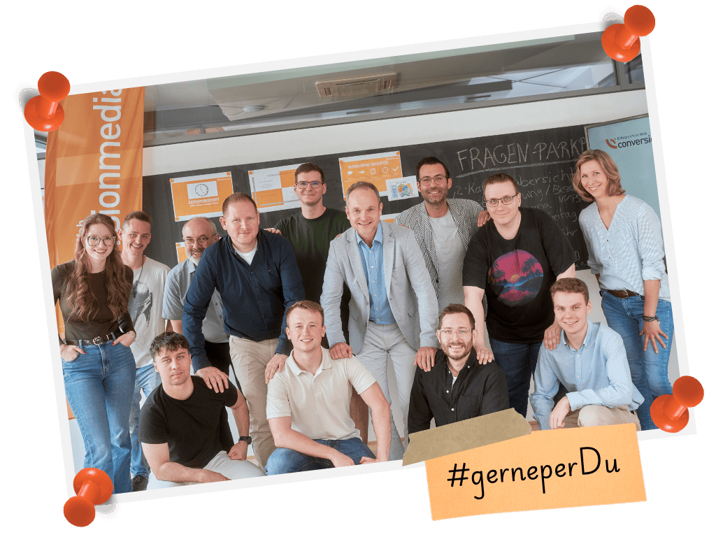 Teamfoto der Conversionmedia vor einer Pinnwand mit Notizen und Hashtag.