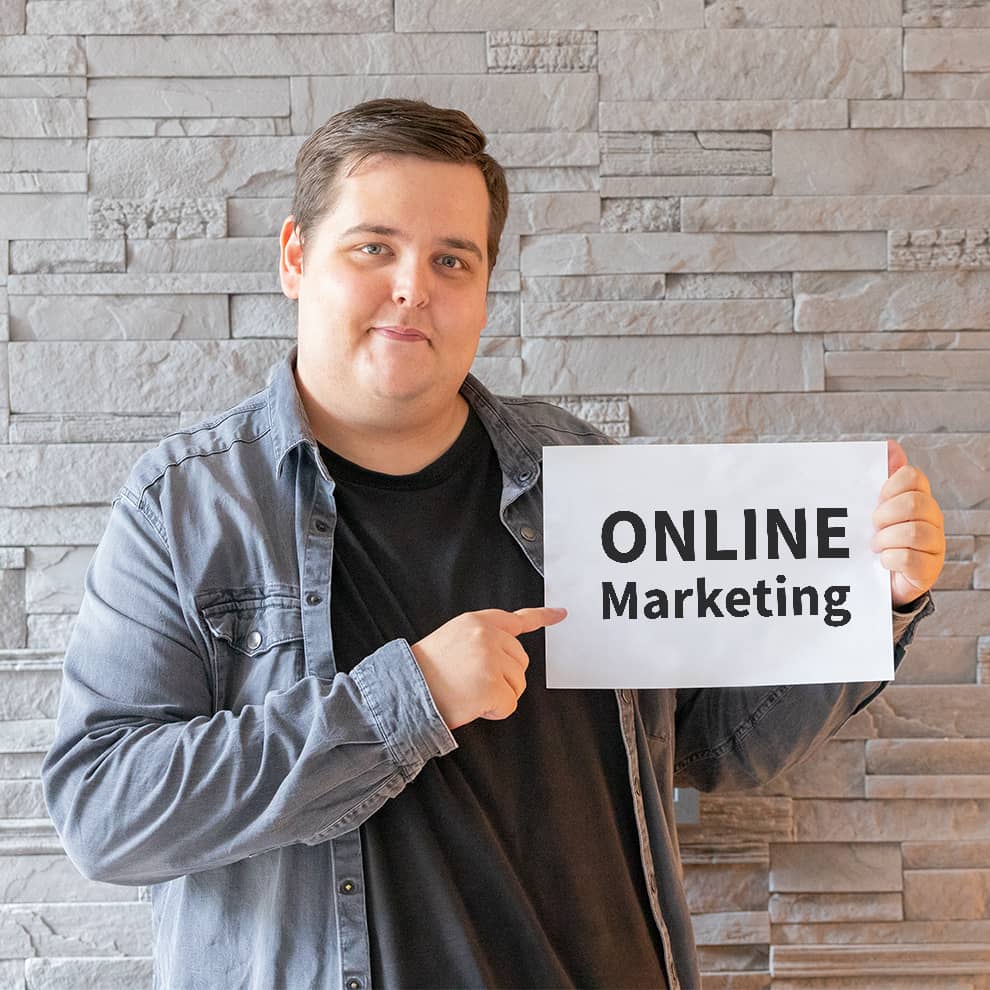 Marcel zeigt auf Papierschild mit Online Marketing