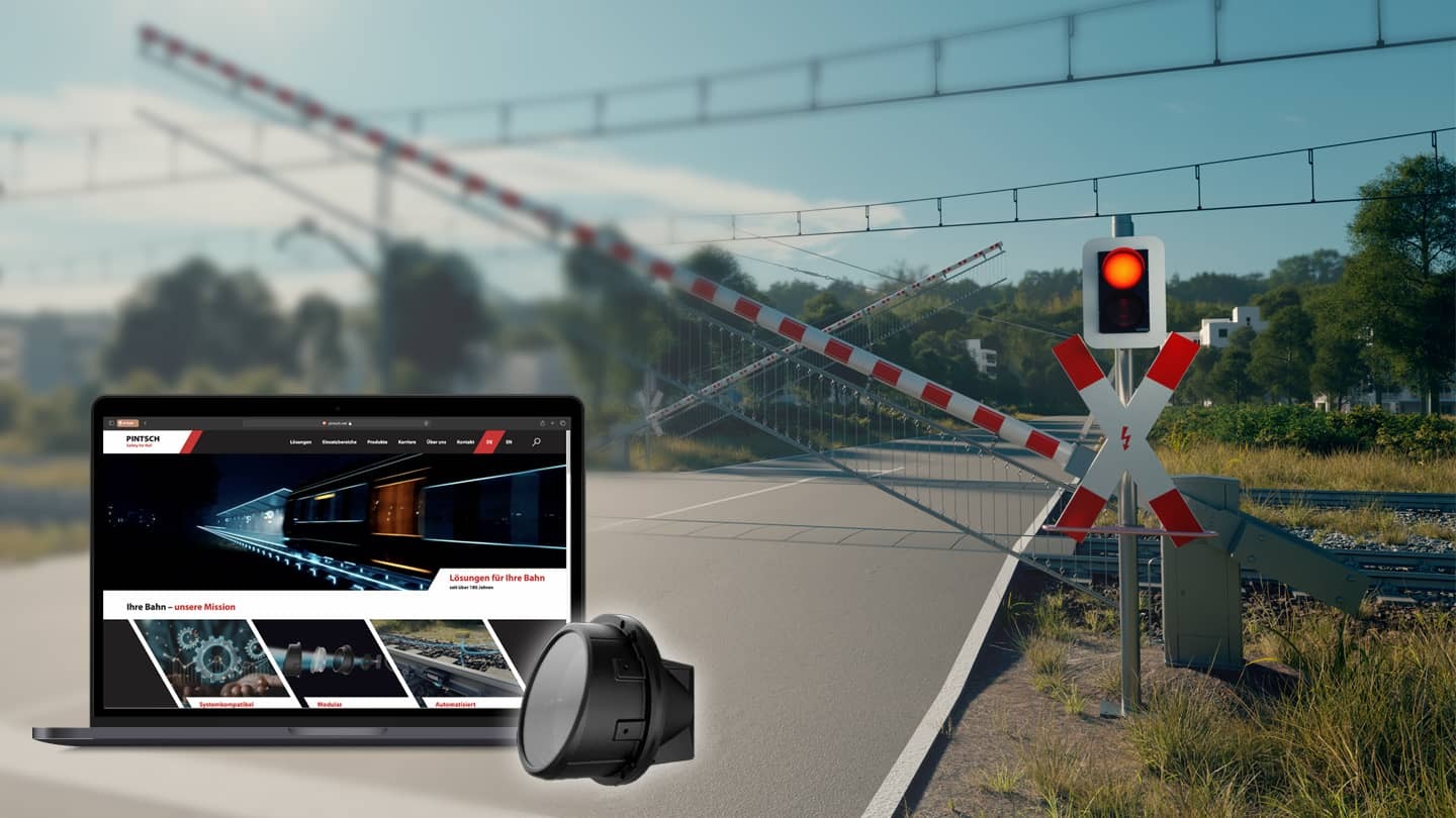 Laptop zeigt die neue PINTSCH Website vor einem Bahnübergang mit rotem Signallicht.
