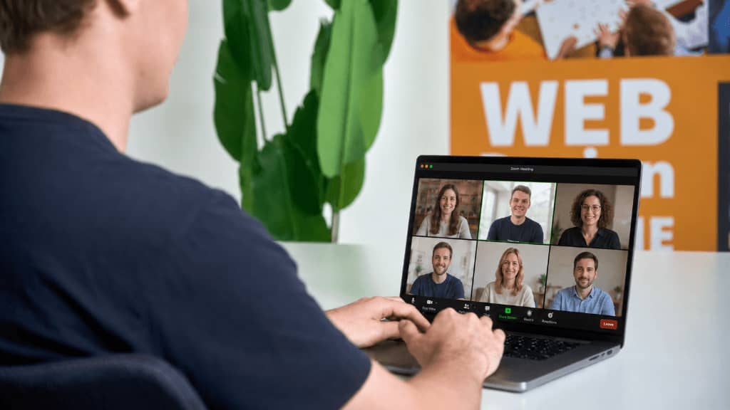 Teilnehmer einer Redakteurschulung arbeiten an einem Laptop in einer Videokonferenz mit sechs sichtbaren Kollegen.