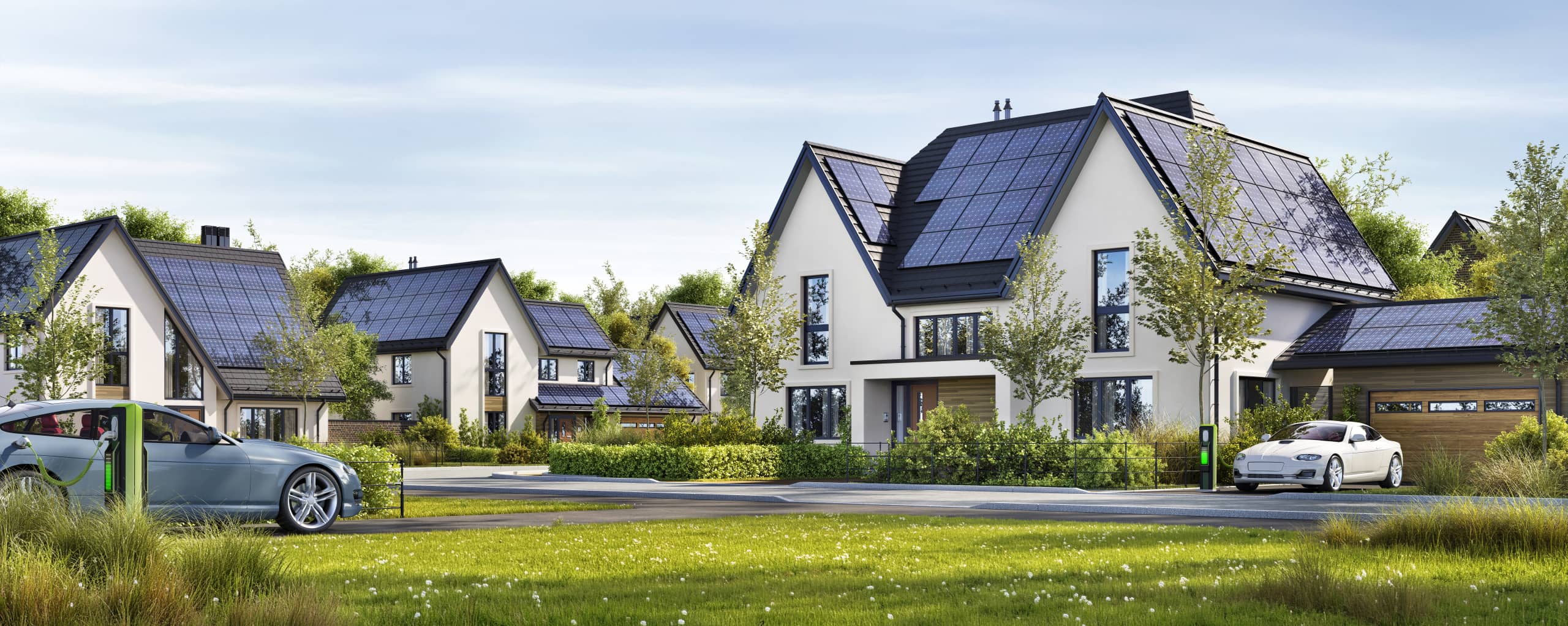 Mehrere zweigeschossige Einfamilienhäuser mit dunklen Solarpaneelen auf den Dächern, Grünflächen und zwei geparkten Elektroautos an der Straße.