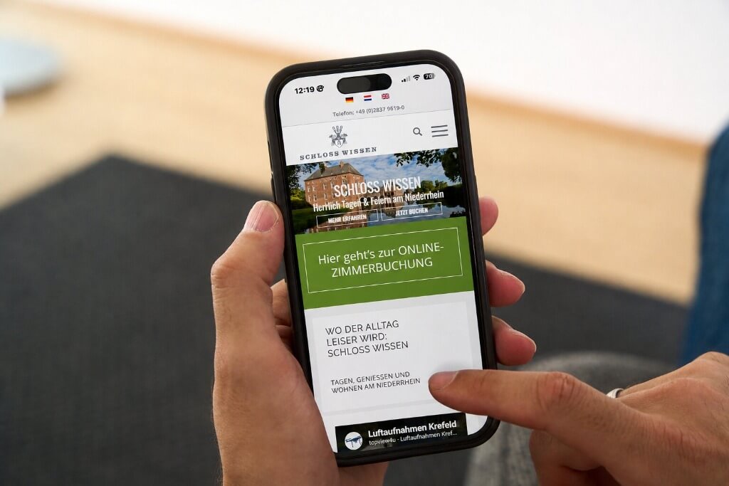 Smartphone zeigt die mobile Webseite von Schloss Wissen mit hervorgehobener Online-Zimmerbuchung.