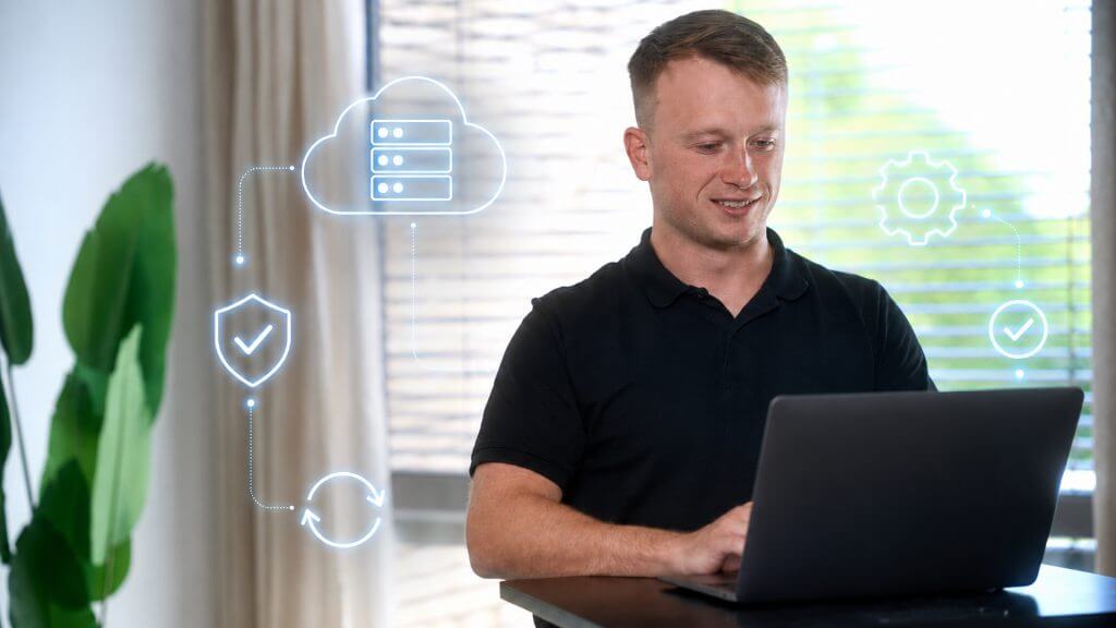 Techniker arbeitet am Laptop vor eingeblendeten Cloud- und Schutzsymbolen, Symbolik für Wartung und Hosting.