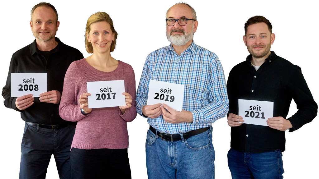 Vier Mitarbeitende halten Schilder mit ihren Eintrittsjahren, zur Illustration von Betriebszugehörigkeit im Jobs-Archiv.