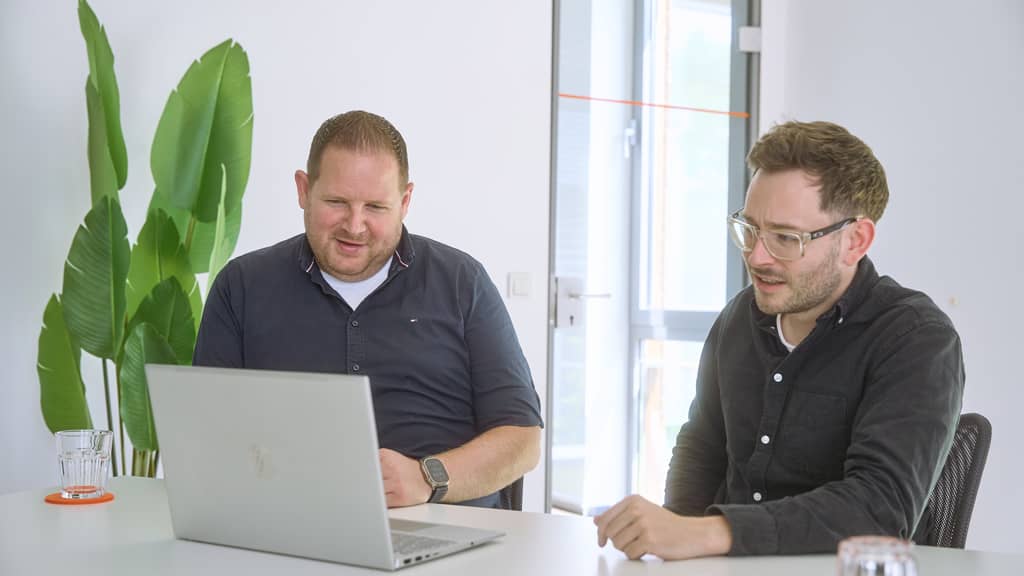 Zwei Personen besprechen am Konferenztisch Inhalte auf einem Laptop.