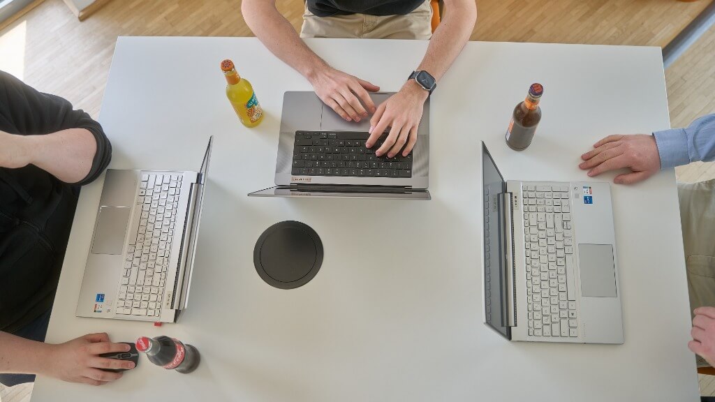 Drei Personen arbeiten mit Laptops an einem Tisch, während Getränke daneben stehen, Sinnbild für Zusammenarbeit bei Website-Optimierung für Empfehlungsgeber.
