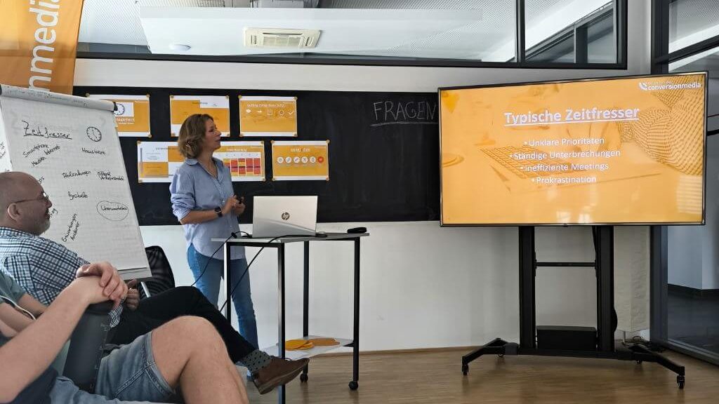 Workshopgruppe diskutiert typische Zeitfresser während eine Präsentation mit Bulletpoints gezeigt wird.